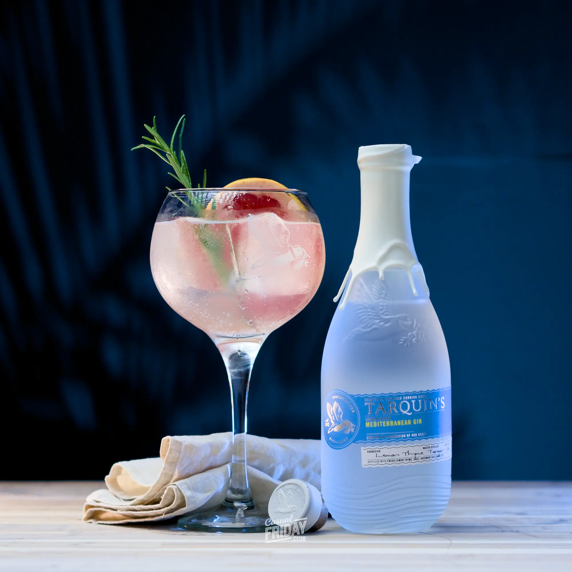 A gin and tonic with rosemary garnish and a grapefruit slice in a copa de balon and a bottle of tarquin's mediterranean gin