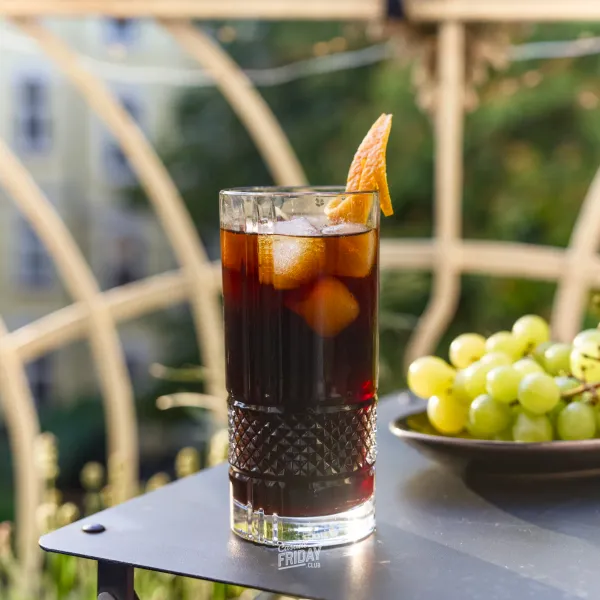 A highball glass with cold brew coffee and ice cubes. Garnished with an orange zest.